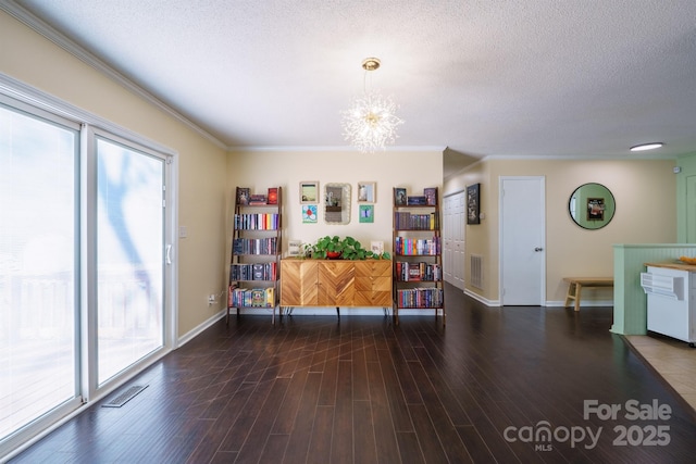 interior space with dark wood-type flooring, ornamental molding, a textured ceiling, and a notable chandelier