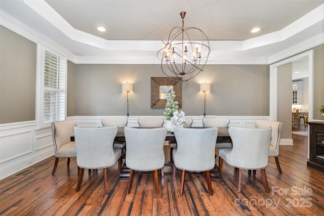 dining room with ornamental molding, an inviting chandelier, a raised ceiling, and dark wood-type flooring