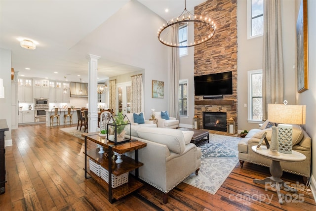 living room featuring a chandelier, a high ceiling, a stone fireplace, and plenty of natural light