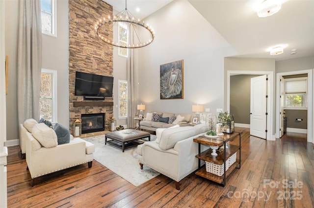 living room featuring dark hardwood / wood-style floors, a stone fireplace, high vaulted ceiling, and a chandelier