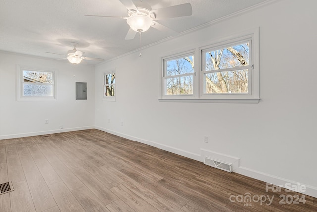 empty room with electric panel, hardwood / wood-style flooring, a wealth of natural light, and ornamental molding