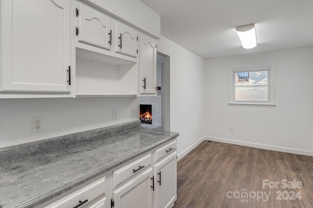 kitchen with white cabinets, a brick fireplace, and dark wood-type flooring