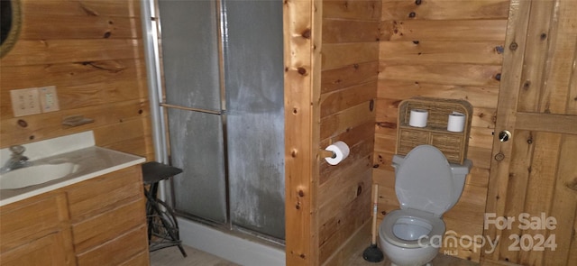 bathroom with an enclosed shower, vanity, toilet, and wooden walls