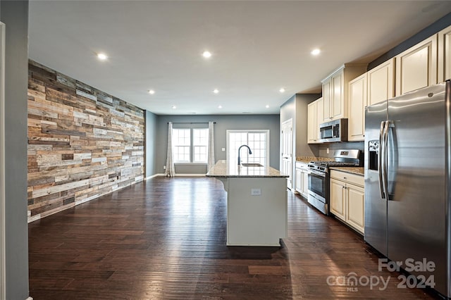 kitchen with a center island with sink, dark hardwood / wood-style floors, light stone counters, and appliances with stainless steel finishes