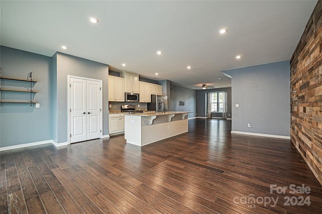 kitchen featuring a center island with sink, stainless steel appliances, dark wood-type flooring, and a breakfast bar area