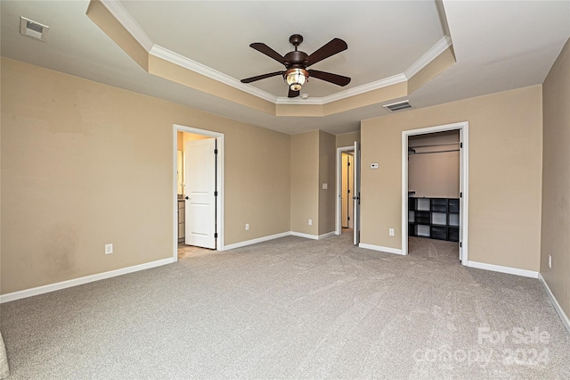 unfurnished bedroom with ornamental molding, a tray ceiling, light colored carpet, ceiling fan, and a spacious closet