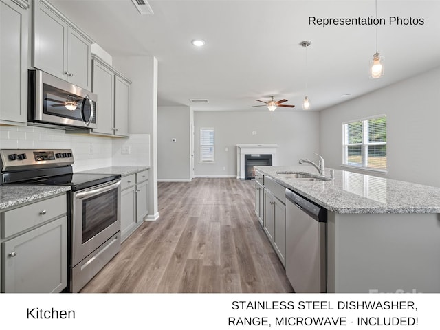 kitchen with sink, hanging light fixtures, gray cabinets, light hardwood / wood-style floors, and stainless steel appliances