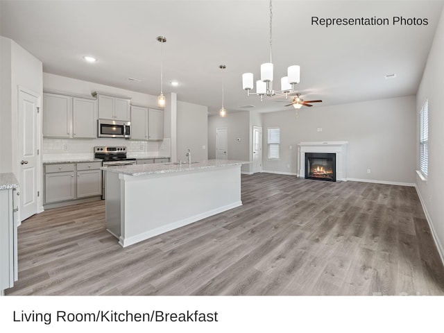 kitchen with gray cabinetry, a kitchen island with sink, light wood-type flooring, appliances with stainless steel finishes, and decorative light fixtures