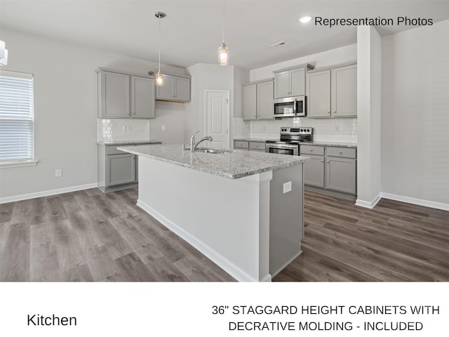 kitchen with appliances with stainless steel finishes, light stone counters, a center island with sink, hardwood / wood-style flooring, and gray cabinets