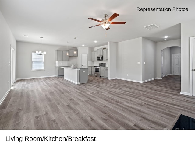 unfurnished living room featuring hardwood / wood-style floors, ceiling fan with notable chandelier, and sink