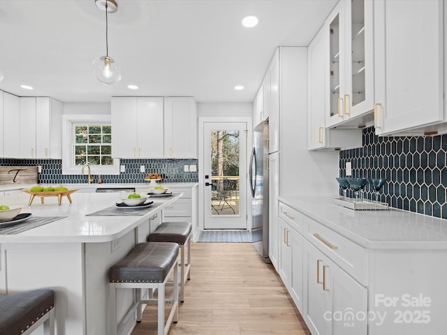 kitchen featuring a kitchen breakfast bar, hanging light fixtures, light hardwood / wood-style floors, white cabinetry, and stainless steel refrigerator