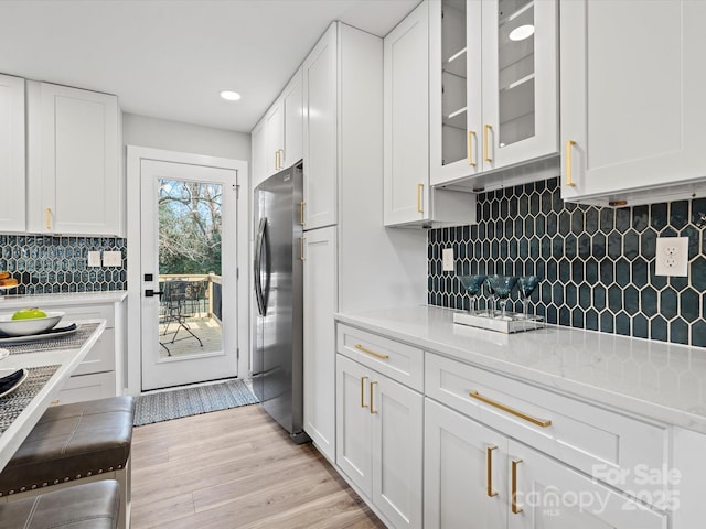 kitchen featuring backsplash, white cabinets, light hardwood / wood-style flooring, light stone counters, and stainless steel refrigerator