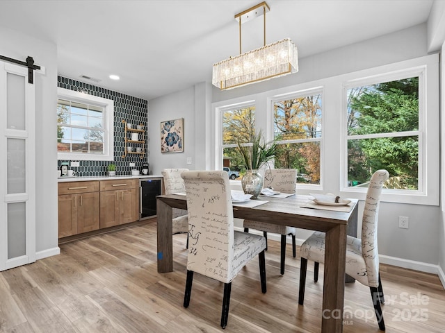 dining space featuring light hardwood / wood-style floors, a barn door, a healthy amount of sunlight, and beverage cooler