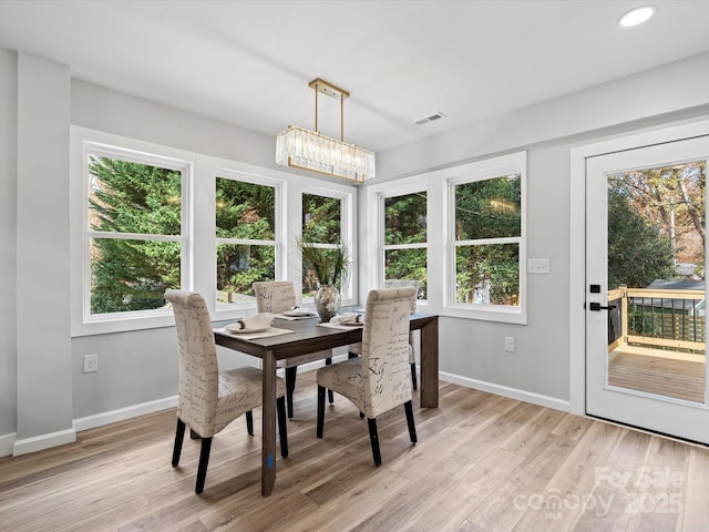 dining area featuring light wood-type flooring, a healthy amount of sunlight, and a notable chandelier