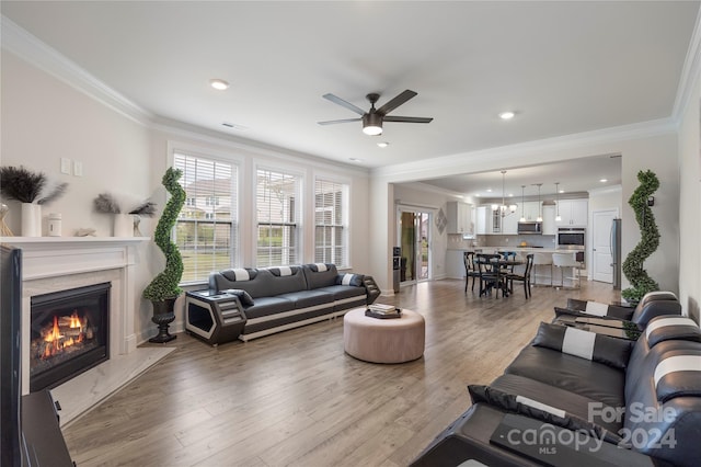 living room with ceiling fan, ornamental molding, a fireplace, and light hardwood / wood-style flooring