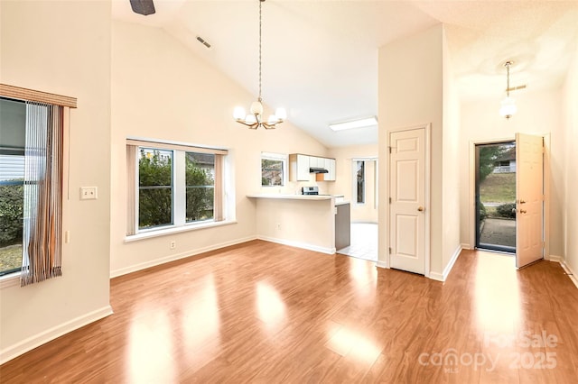 unfurnished living room featuring ceiling fan with notable chandelier, light hardwood / wood-style flooring, and high vaulted ceiling