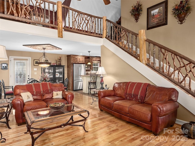 living area with stairs, light wood-type flooring, a towering ceiling, and a healthy amount of sunlight