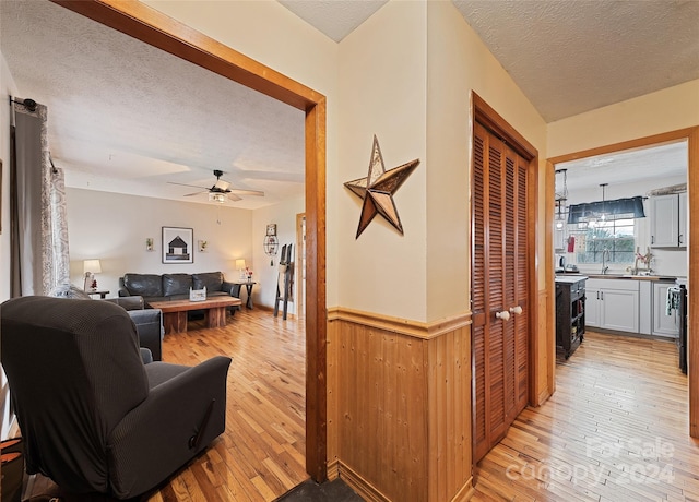 living room with ceiling fan, light wood-type flooring, a textured ceiling, and wooden walls