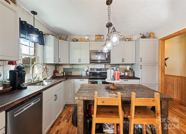 kitchen with appliances with stainless steel finishes, sink, a center island, light hardwood / wood-style floors, and wood walls