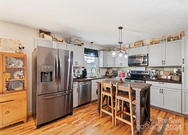 kitchen featuring sink, stainless steel appliances, pendant lighting, light hardwood / wood-style floors, and white cabinets