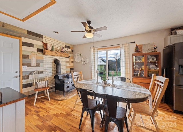 dining space featuring ceiling fan, light wood-type flooring, a textured ceiling, and a wood stove