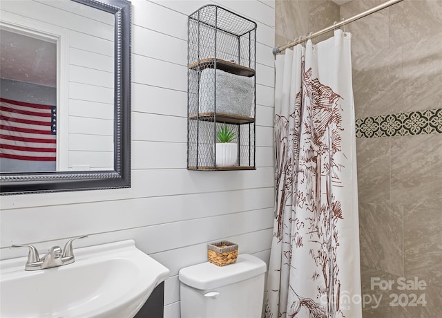 bathroom with a shower with curtain, toilet, sink, and wooden walls