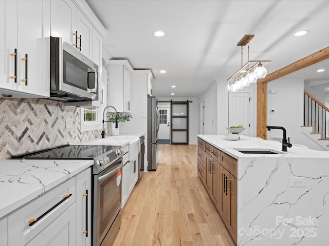 kitchen featuring sink, decorative light fixtures, appliances with stainless steel finishes, a barn door, and white cabinets