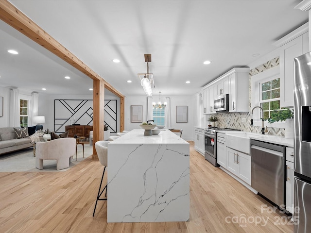 kitchen with pendant lighting, stainless steel appliances, a kitchen island, and white cabinets