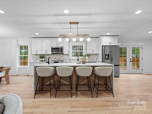 kitchen featuring appliances with stainless steel finishes, white cabinetry, hanging light fixtures, a center island with sink, and french doors