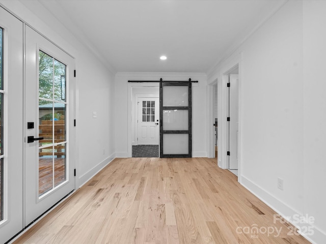 interior space with crown molding, a barn door, and light wood-type flooring