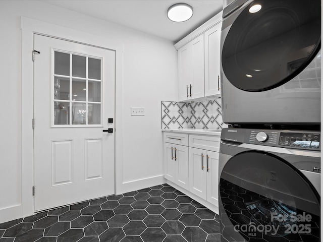 clothes washing area with cabinets, stacked washing maching and dryer, and dark tile patterned floors