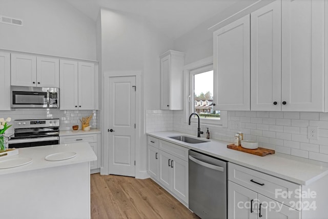 kitchen featuring tasteful backsplash, stainless steel appliances, sink, white cabinets, and light hardwood / wood-style floors