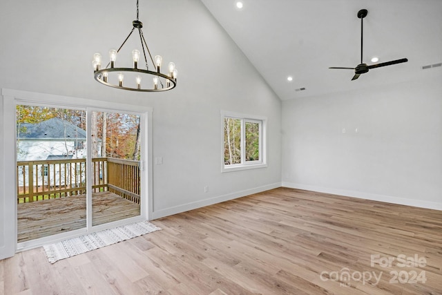 unfurnished dining area with high vaulted ceiling, ceiling fan with notable chandelier, and light wood-type flooring