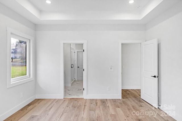 unfurnished bedroom featuring a tray ceiling, ensuite bath, and light hardwood / wood-style flooring