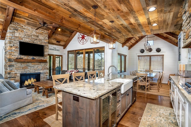 kitchen featuring sink, dark wood-type flooring, hanging light fixtures, a kitchen island with sink, and a fireplace