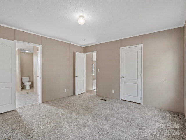 unfurnished bedroom with connected bathroom, light carpet, and a textured ceiling