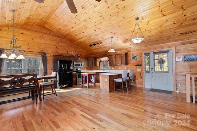 kitchen with decorative light fixtures, stainless steel appliances, light hardwood / wood-style flooring, and wooden walls