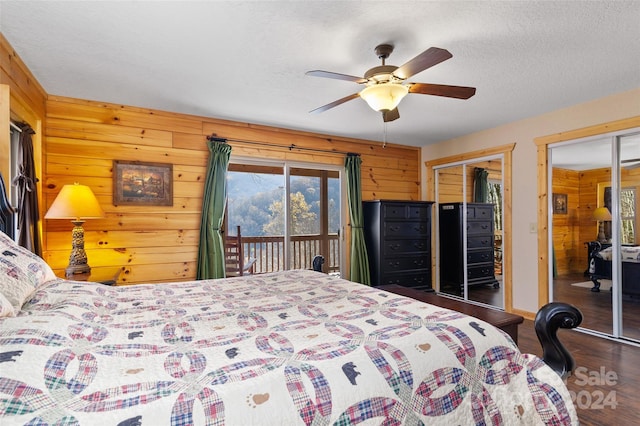 bedroom with wood walls, two closets, ceiling fan, access to exterior, and dark hardwood / wood-style flooring