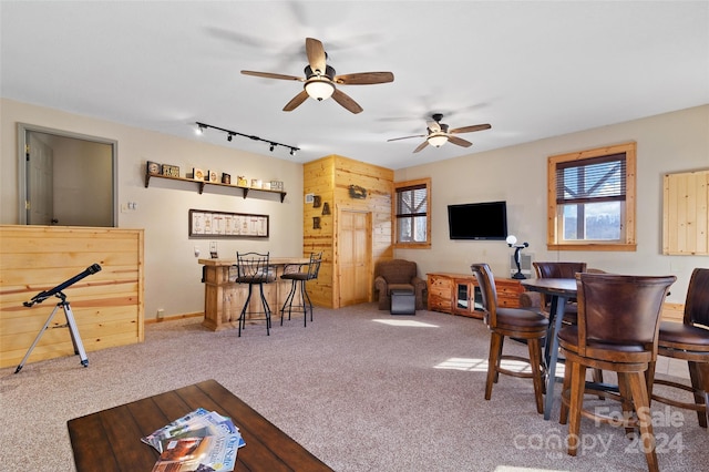 dining space featuring carpet flooring, bar, track lighting, and ceiling fan