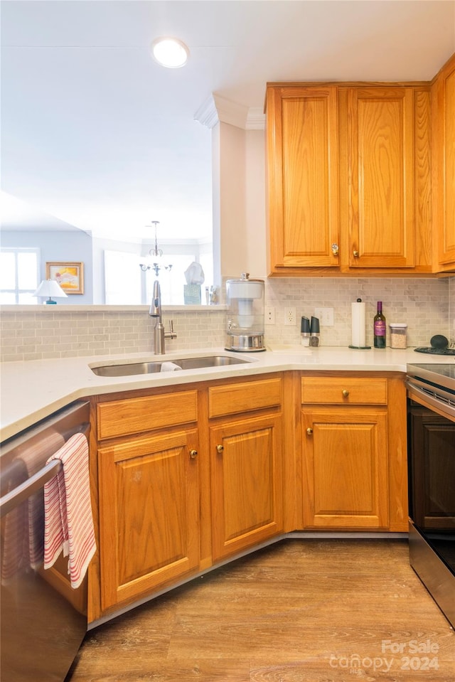 kitchen with appliances with stainless steel finishes, backsplash, sink, a chandelier, and light hardwood / wood-style floors