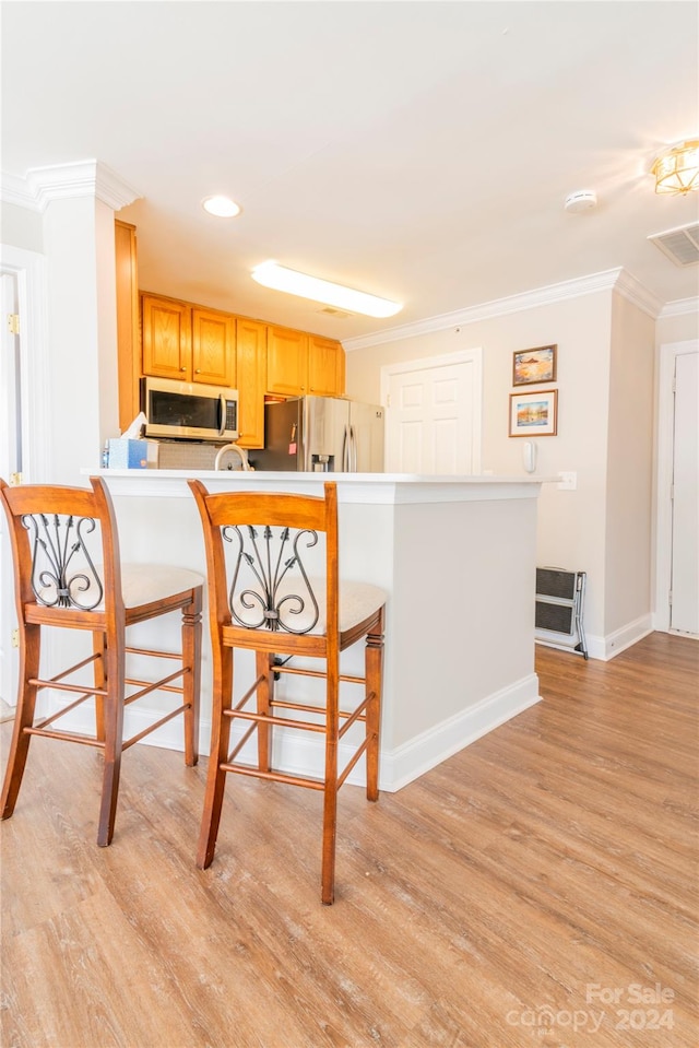 kitchen with kitchen peninsula, appliances with stainless steel finishes, ornamental molding, a breakfast bar, and light hardwood / wood-style floors