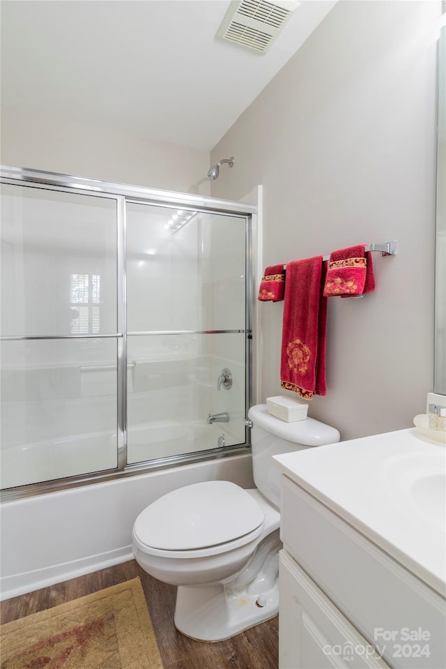 full bathroom featuring vanity, hardwood / wood-style flooring, toilet, and bath / shower combo with glass door