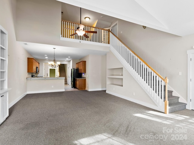 unfurnished living room featuring carpet flooring, ceiling fan with notable chandelier, a towering ceiling, and built in shelves