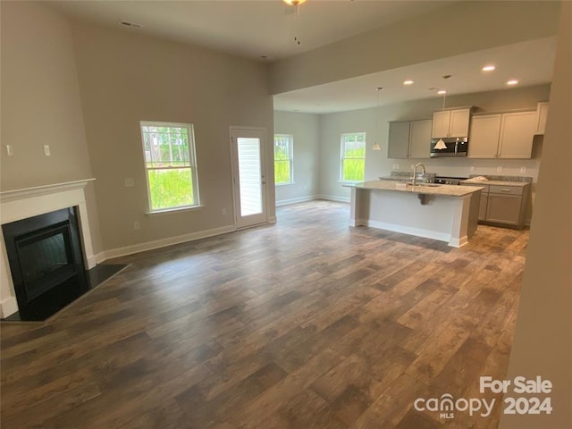 kitchen with gray cabinetry, sink, dark wood-type flooring, a breakfast bar area, and a center island with sink