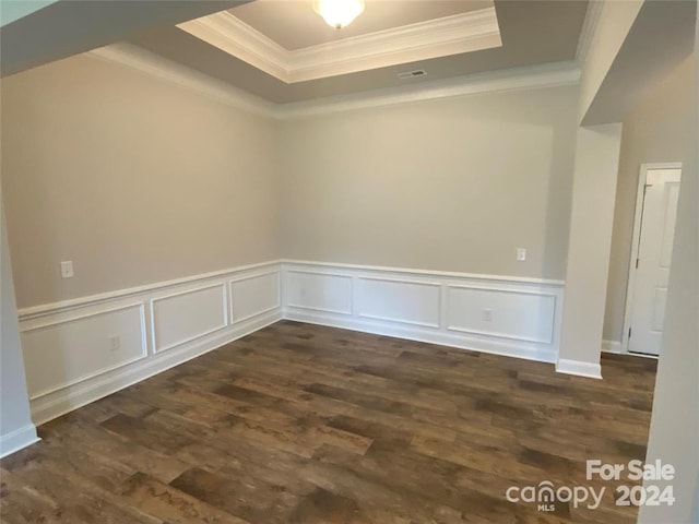 unfurnished room with a raised ceiling, crown molding, and dark wood-type flooring