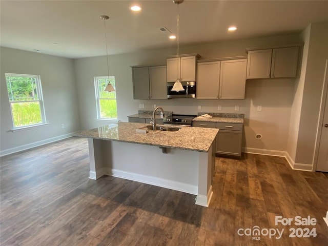 kitchen with sink, hanging light fixtures, light stone counters, dark hardwood / wood-style floors, and a center island with sink