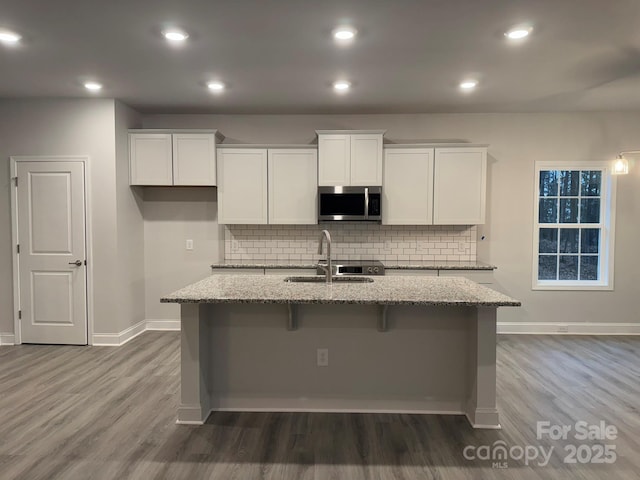 kitchen featuring white cabinetry, a kitchen island with sink, sink, and light stone counters