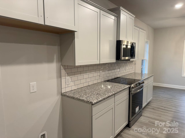 kitchen with backsplash, light stone countertops, light hardwood / wood-style floors, and appliances with stainless steel finishes