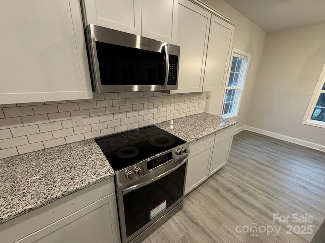 kitchen featuring white cabinetry, stainless steel appliances, light stone counters, light hardwood / wood-style floors, and decorative backsplash