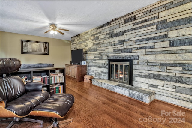 living room featuring hardwood / wood-style floors, a textured ceiling, a stone fireplace, and ceiling fan